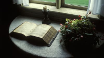 En mycket gammal bok ligger uppslagen på ett bord intill ett fönster.