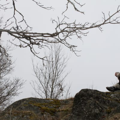 Nainen mietiskelee kevätsäässä kalliolla.