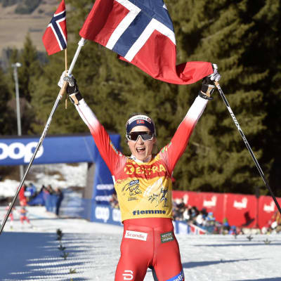 Therese Johaug jublar med den norska flaggan då hon korsar mållinjen.