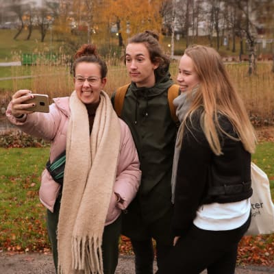 Tre ungdomar, en pojke och två flickor, i en grupp som tar en selfie.