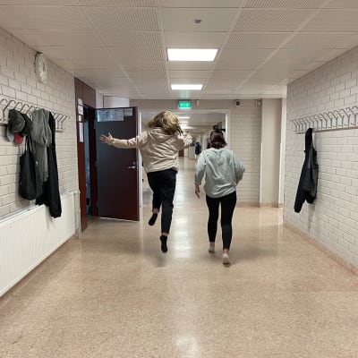 Tytöt juoksevat ja hyppelevät yläkoulun tyhjällä käytävällä