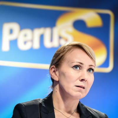 Hanna Mäntylä med Sannfinländarnas logo i bakgrunden.
