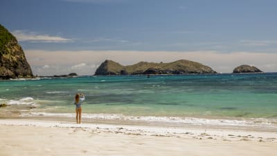 Nancy (Blake Lively) står på en öde sandstrand och fotograferar havet och en stor ö ute vid horisonten.