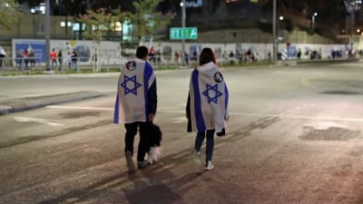 Ett ungt par insvepta i israeliska flaggor går längs en öde gata tillsammans med sin hund.