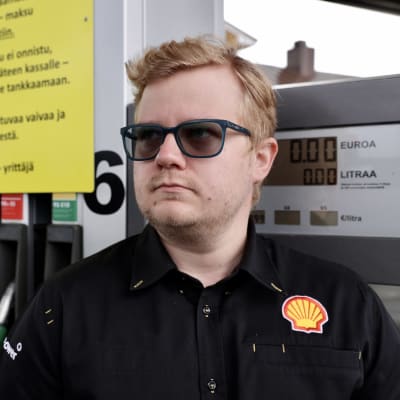 Aurinkolasipäinen mies seisoo tankkausaseman vieressä. Mustassa paidassa Shellin logo.