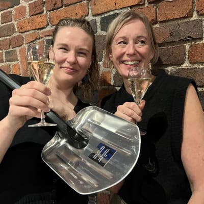  Anu Rummukainen och Jessica Stolzmann visar upp sitt snöspade-pris och håller två skumvinsglas i händerna. 