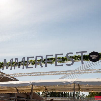 Tammerfest-tapahtuma-alueen sisäänkäynnin mainoskyltti. Kyltissä viherkasveja ja teksti "Tammerfest".