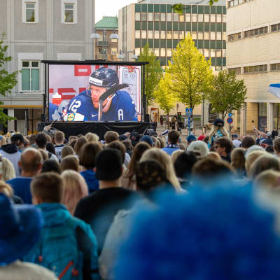 Aurinkoinen Keskustori täynnä ihmisiä seuraamassa peliä screeniltä.