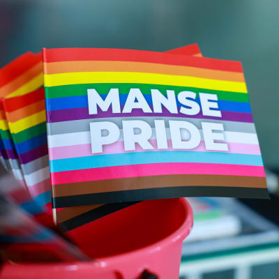 Pieni ja värikäs pride-lippu, jossa valkoisella teksti "Manse Pride".