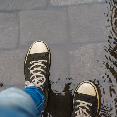 Ett par jeansklädda ben och sneakers syns av en person som går i en vattenpöl.