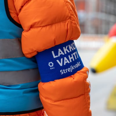 Närbild av ett band på en rock där det står "strejkvakt".