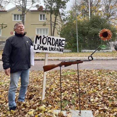 Mosse Wallén står bakom en fredsskupltur som är gjord ab en gammal bössa med en knut på pipan och en solros i ändan. 