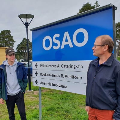 OSAO:n toisen vuoden opiskelija Eemeli Telkki ja metsäalan lehtori Ilpo Pennanen Muhoksen OSAO-kyltin edessä. 