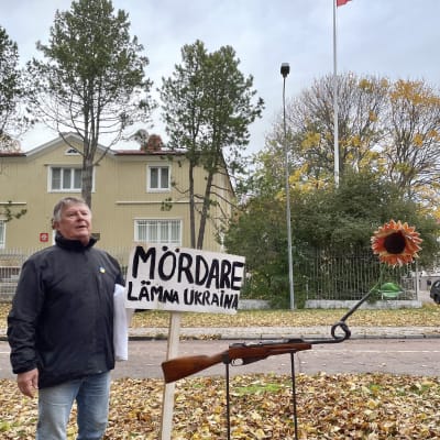 Mosse Wallén står bakom en fredsskupltur som är gjord ab en gammal bössa med en knut på pipan och en solros i ändan. 