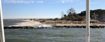 Flörbindelsebåten sveper förbi en strand somo skyddas av en stenmur.