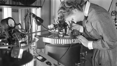 Lotta-pukuinen nainen työssä pikalevyjen äänityslaitteen äärellä 1940-luvulla. Ääniä ja radio-ohjelmia tallennettiin sellakkakalvopintaisille metallilevyille.