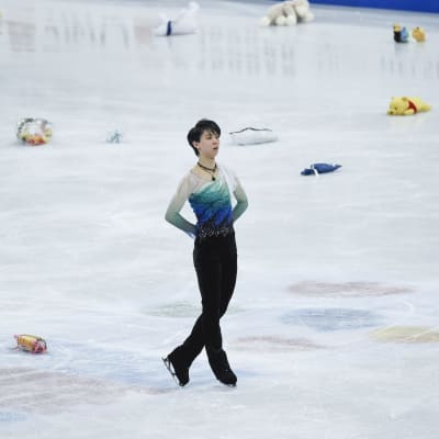 Konståkaren Yuzuru Hanyu står på isen som täcks av nallar och blommor.