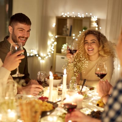 Fyra leende personer vid ett matbord. De har vinglas i händerna och på bordet finns många stearinljus. I bakgrunden en hylla och ljusslingor.