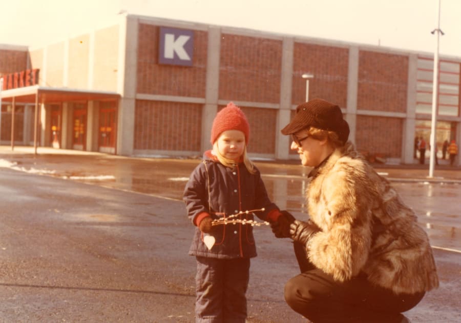 Toimittaja, kirjailija Meri Eskola äitinsä kanssa Helsingissä Itäkeskuksen vanhan Citymarketin edustalla pääsiäisenä 1978. Punapipoisella Merillä pajunkissoja kädessään, äidillä turkki yllään. Äiti pitää Meriä kädestä.