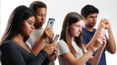 Fyra unga personer försjunkna i sina mobiltelefoner.