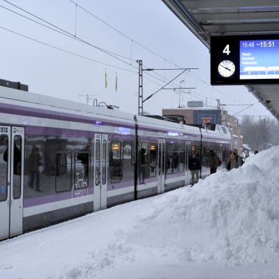 Snöhög på tågstation, invid tåg som står stilla. 