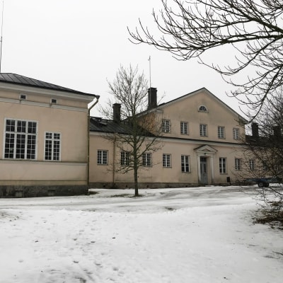 Ett stort gult stenhus, huvudbyggnaden vid Själö gamla sjukhus, med snö på marken.