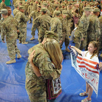 Amerikkalainen sotilas halaa vaimoaan, sotilaan tytär odottaa vieressä tervetulolipun kanssa. 