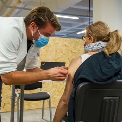 Sjukskötaren Antti Laitinen ger en kvinna ett vaccin i Busholmens vaccineringsställe.