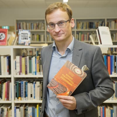 forskningsprofessor Mikael Mattlin håller upp en bok.