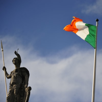 Irlands flagga i orange, vitt och grönt framför en gammal staty i Dublin.
