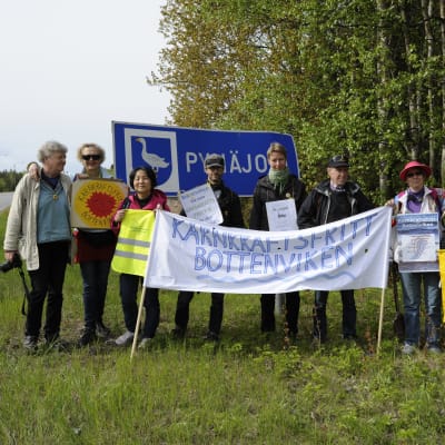 Gruppfoto på rikssvensk kärnkraftsdemonstraner med banderoll och flaggor i Pyhäjoki invid Europaväg 8.