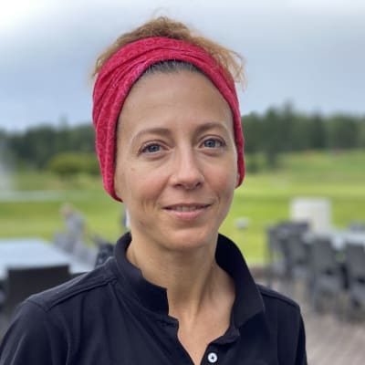 Yngre kvinna i röd huvudbonad står vid sidan av golfplan.