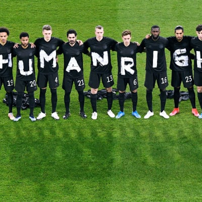 Jalkapalloammattilaiset seisovat nurmikentällä ja heidän paidoissaan on kirjaimet, joista muodostuu sana humanrights.