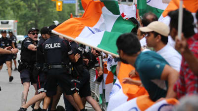 Poliser samlas kring en demonstrant. Indiska flaggor viftas.
