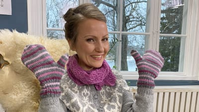 Kvinna sitter i en korgstol och har vantar på händerna som hon visar upp