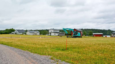 En grusväg kantad av gräs och några enstaka hus samt en grävmaskin.
