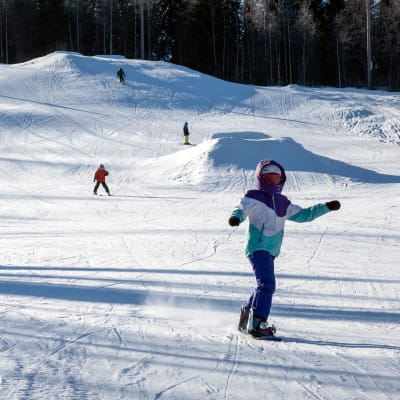 Lapset laskevat mäkeä laskettelusuksilla ja lumilaudoilla Pukkivuoren laskettelurinteessä.