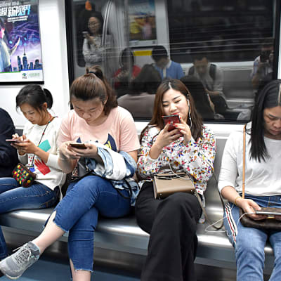 Kineser surfar på mobiltelefonen i ett tåg