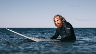 Karaktären Erik sitter på sitt surfbräde ute till havs.