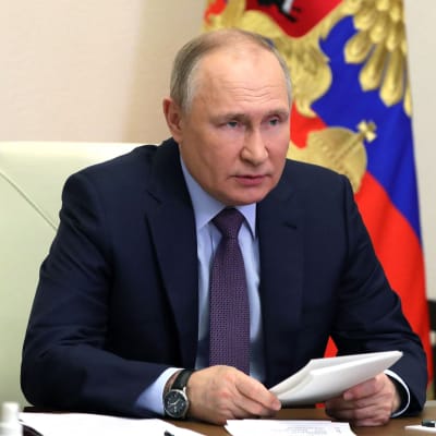 Rysslands president Vladimir Putin sitter vid ett arbetsbord och håller i ett vitt häfte.