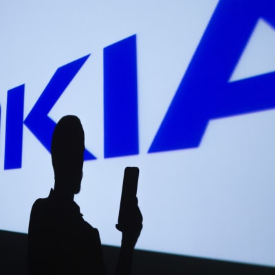 Nokias logo i bakgrunden. I förgrunden syns en person som håller i en telefon.