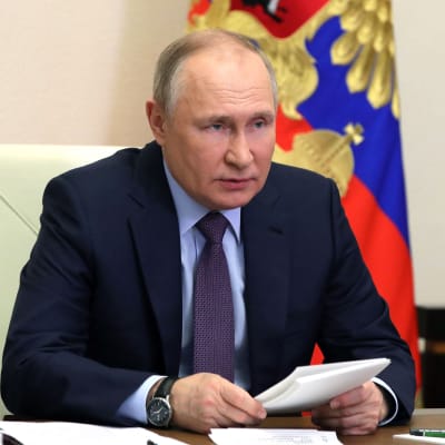 Rysslands president Vladimir Putin sitter vid ett arbetsbord och håller i ett vitt häfte.