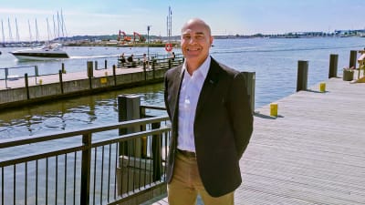 Ilkka Matila står på en brygga och ler medan han tittar in i kameran.
