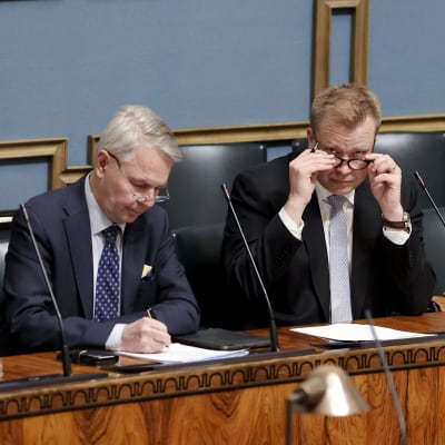 Två män i kostym sitter vid ett långt arbetsbord i Finlands riksdag.
