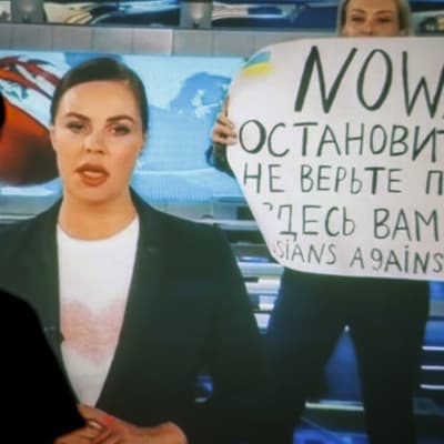 Protest mot kriget i rysk statsstyrd TV, en kvinna bakom nyhetsankaret håller i en skylt med texten "Nej till krig".