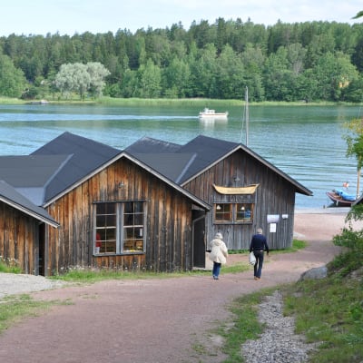 I förgrunden båtmuseet i Näsby med sina låga hus, i bakgrunden den blå Hålaxviken.