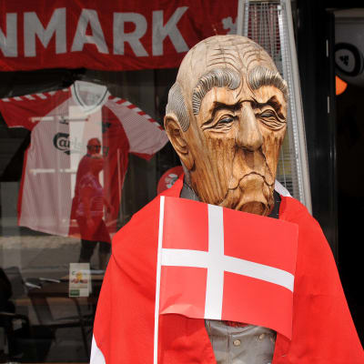 Puusta tehty mies pitelee pientä Tanskan lippua. Patsaan harteilla on Tanskan lippu.