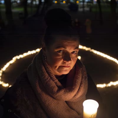 En kvinna står i mörker med ett gravljus i handen.