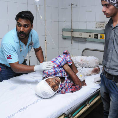 En skadad man med bandage runt huvudet ligger på en sjukhussäng, medan sjukvårdspersonal jobbar runt honom.