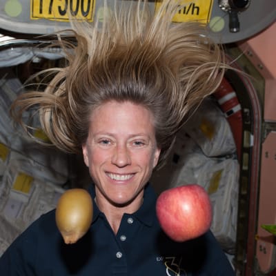 Astronautti Karen Nyberg hymyilee kuvassa ja hänen edessään leijuu kaksi hedelmää painovoimattomassa tilassa kansainvälisellä avaruusasemalla
